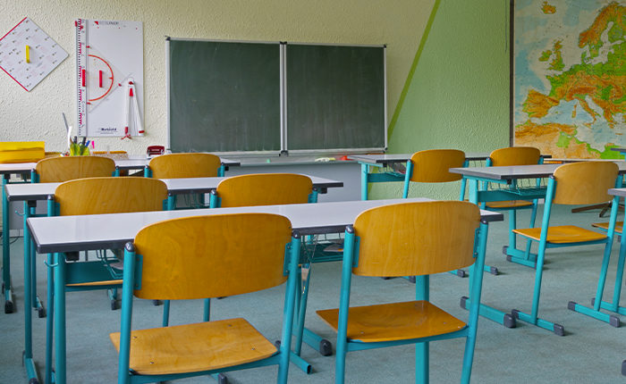 Salle de classe vide avec des bureaux et des chaises d’élèves qui font face à un tableau noir. Une carte du monde est affichée sur le mur de droite.