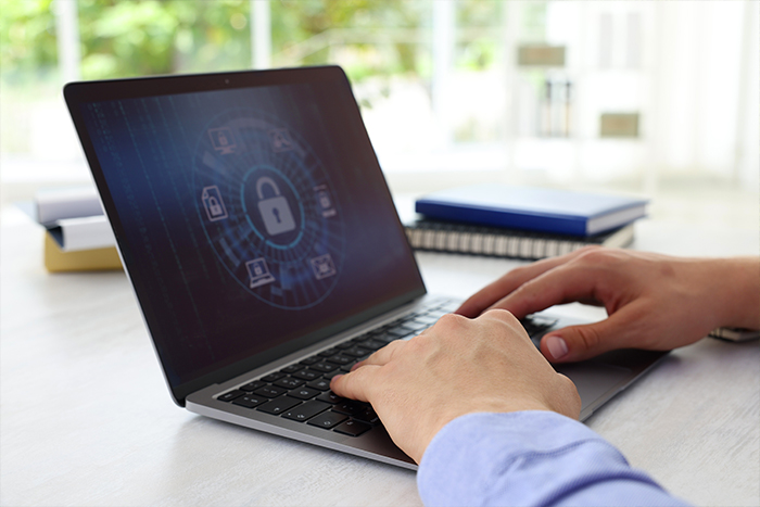 Photo des mains d'une personnes tapant sur un clavier d'ordinateur. Un cadenas entouré d'autres dessins aux alentours sont visibles sur l'écran.