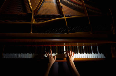 Deux mains photographiées en hauteur en train de jouer du piano.