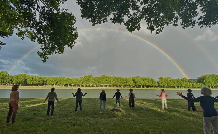 Personnes pratiquant le qi gong en plein air devant un lac et avec un arc-en-ciel en premier plan