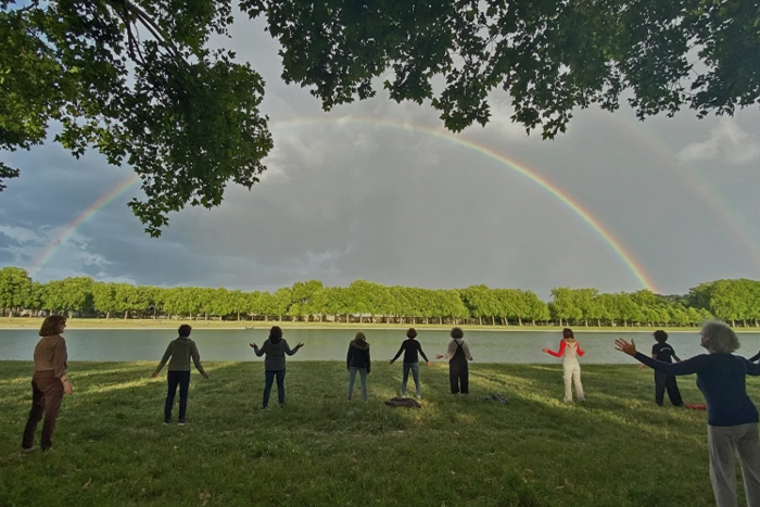 Personnes pratiquant le qi gong en plein air devant un lac et avec un arc-en-ciel en premier plan